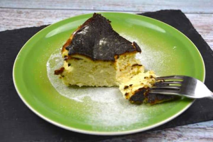 Authentic Basque burnt cheesecake slice with a deeply caramelized top serving on a green plate.