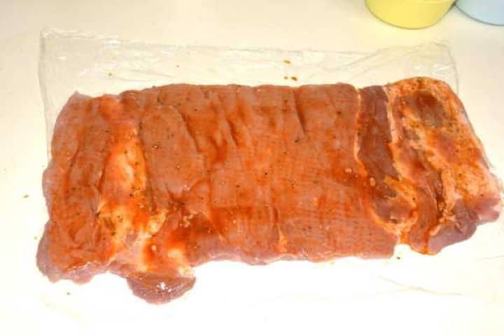 Butterflying a boneless pork loin horizontally with a sharp chef's knife on a cutting board.
