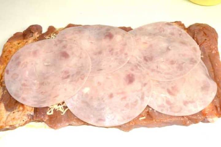 Assembling roasted red peppers, grated mozzarella cheese, and smoked ham slices over butterflied pork loin.