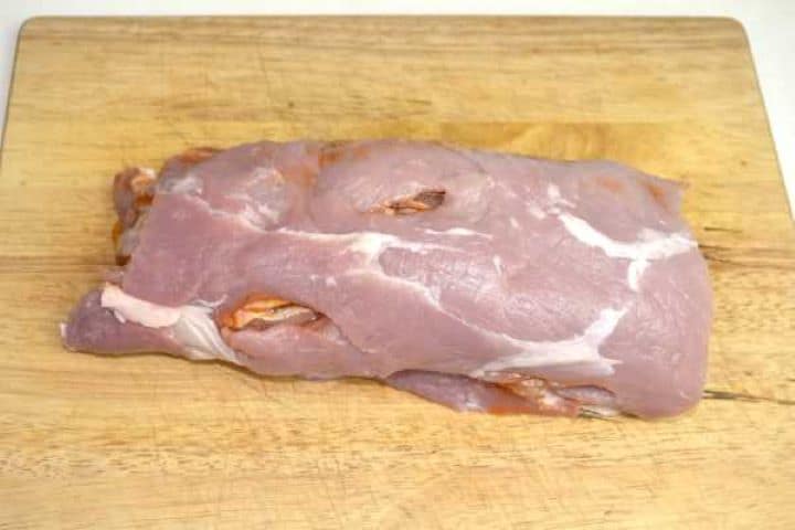 Brushing garlic honey baste over butterflied pork loin before rolling to marinate at room temperature.