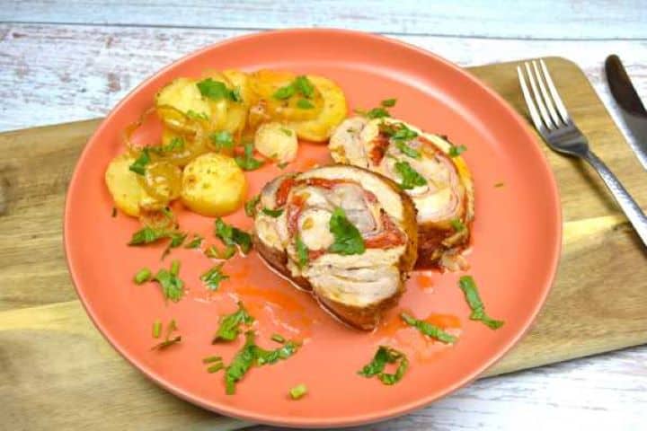 Carving warm ham and cheese stuffed pork loin into thick slices showing the melted cheese and red pepper spiral.