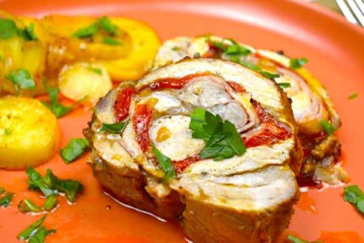 Delicious ham and cheese stuffed pork loin slice served on orange plate with baked onion and potatoes.