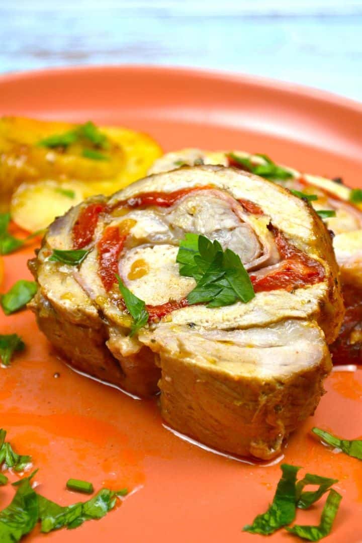 Juicy ham and cheese stuffed pork loin sliced into pinwheels served with roasted potatoes on a platter.