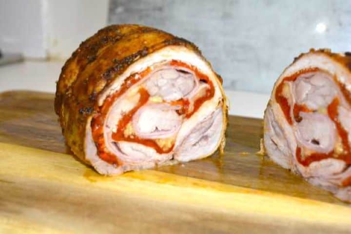 Carving rested ham and cheese stuffed pork loin into thick pinwheel slices showing juicy meat and melted cheese.