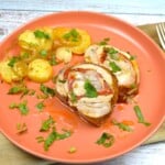 Sliced ham and cheese stuffed pork loin roast displaying melted mozzarella spiral served with roasted potatoes.