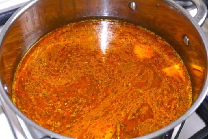 Spiced carrot and red lentil soup simmering in liquid in a pot on the stove.