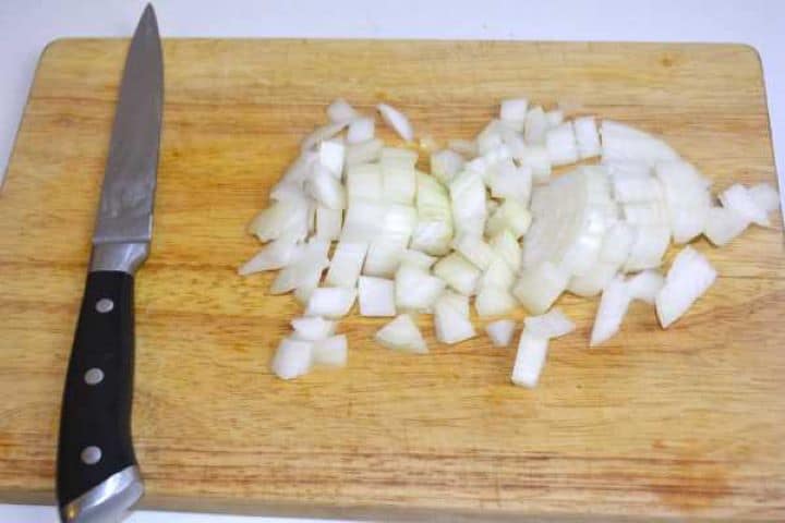 Finely diced yellow onion and minced fresh garlic on a wooden chopping board.