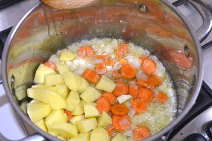 Adding sliced carrots and cubed potatoes to softened onions in the soup pot.