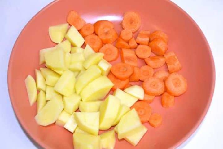 Peeled sliced fresh carrots and cubed potatoes on a plate prepared for lentil soup.