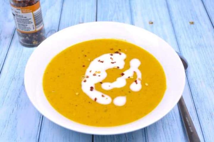 Golden bowl of spiced carrot and lentil soup garnished with coconut milk and red pepper flakes.