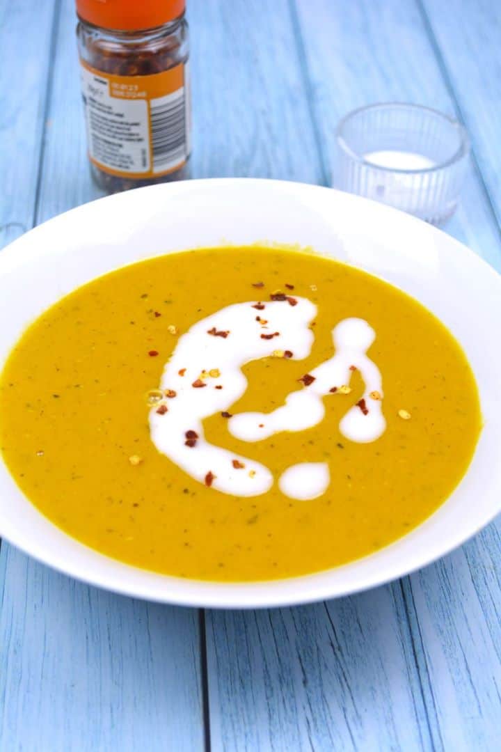 Velvety creamy carrot and red lentil soup served in a white bowl with a coconut milk swirl and chili flakes.