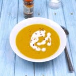 Velvety creamy carrot and red lentil soup served in a white bowl with a coconut milk swirl and chili flakes.