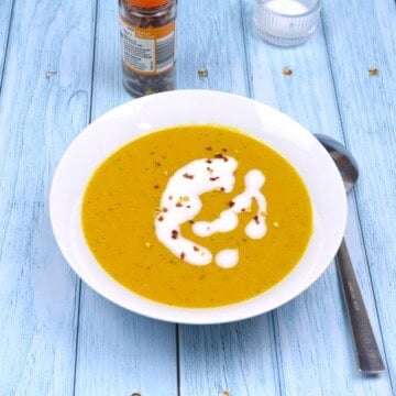 Velvety creamy carrot and red lentil soup served in a white bowl with a coconut milk swirl and chili flakes.