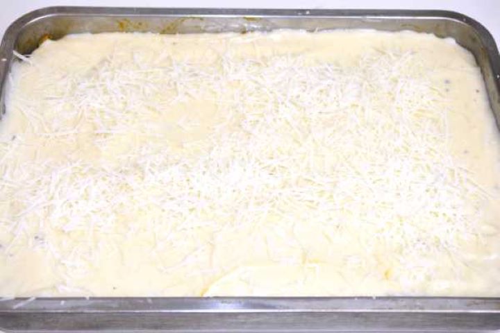 Spreading thick béchamel sauce over the meat layer of a Greek moussaka.