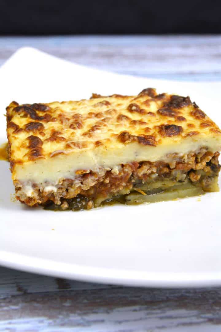 Authentic Greek moussaka slice with eggplant and potatoes on a white plate.