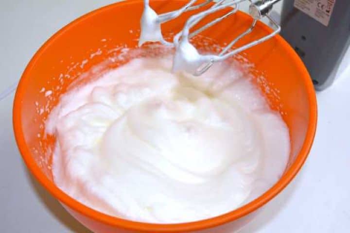 Egg whites beaten to stiff, glossy peaks in a mixing bowl for sponge cake batter.