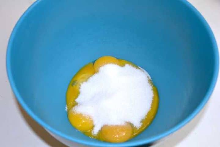Separated egg yolks and granulated sugar in a blue mixing bowl.