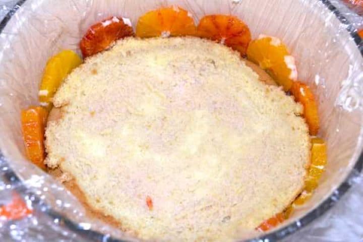 Placing sliced sponge cake over diplomat cream and drizzling with fresh orange syrup.
