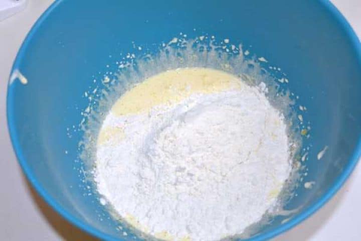 Sifted flour and baking powder resting on top of whipped egg yolk mixture in a bowl.