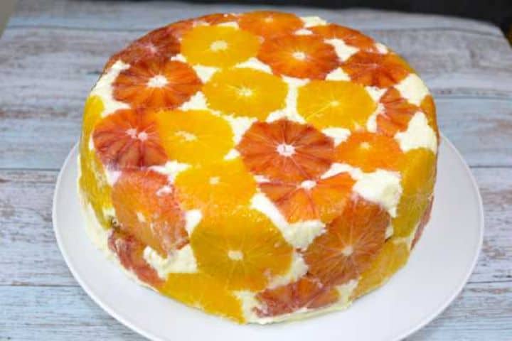 Chilled upside down orange cake with a fresh orange slice mosaic topping on a white serving plate.