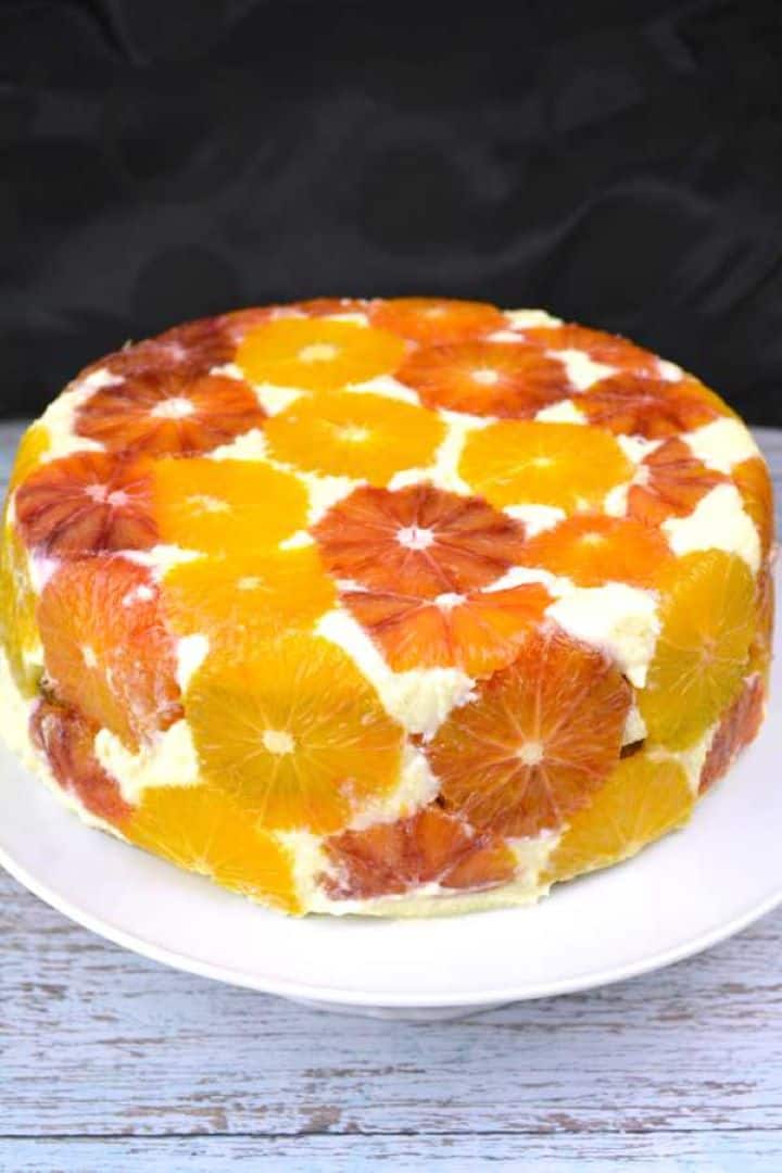 Chilled upside down orange cake with a fresh orange slice mosaic topping on a white serving plate.