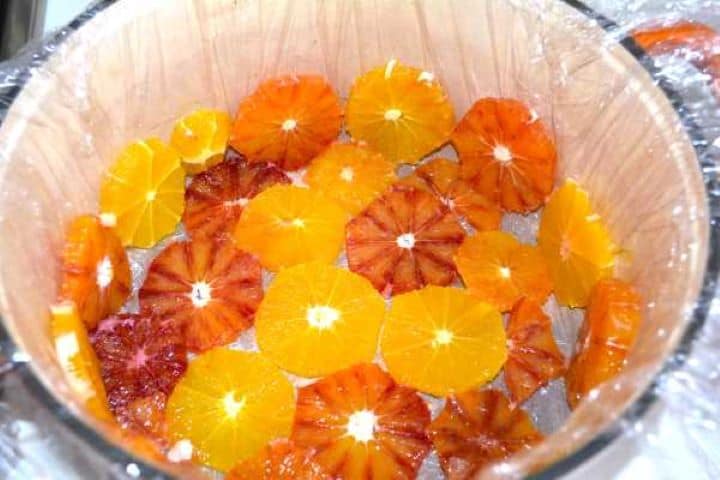 Arranging macerated orange slices in a mosaic pattern on the bottom of a foil-lined pot.