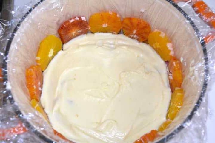 Spreading a layer of silky diplomat cream over sliced oranges in a lined Dutch oven.
