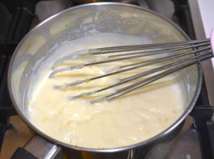 Thick vanilla and orange pastry cream cooking over medium heat in a stainless steel saucepan.