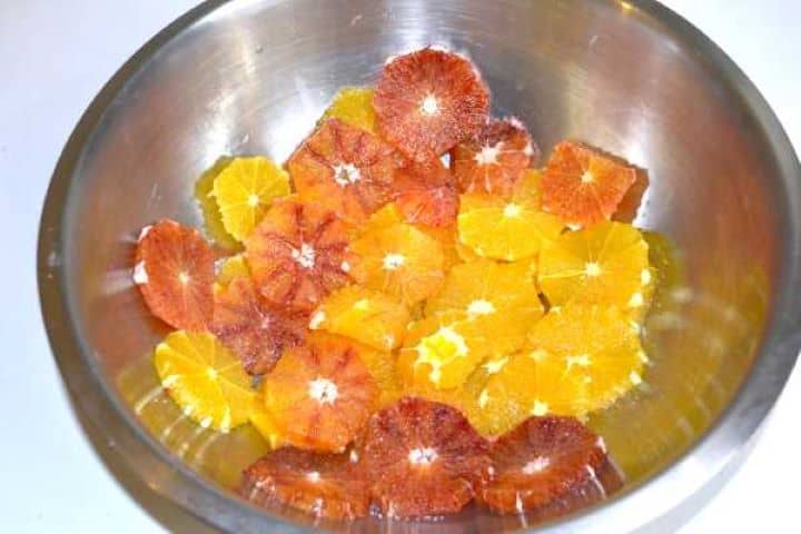 Thin orange slices resting with sugar in a bowl to extract fresh citrus soaking syrup.