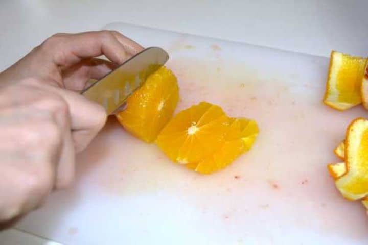 Slicing fresh peeled oranges into thin rounds on a white cutting board.