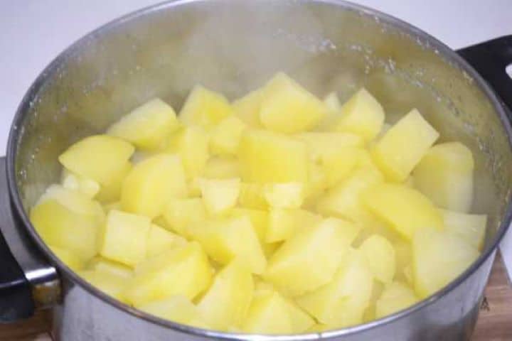Drained fork-tender boiled potatoes in a stainless steel pot ready to be crushed.