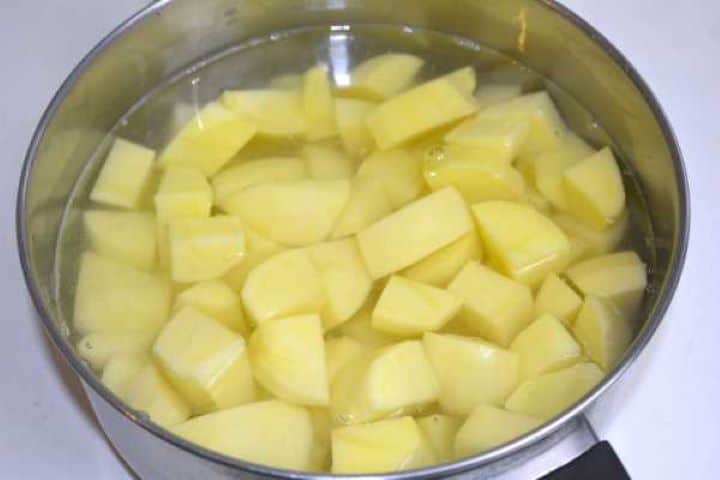Peeled and diced potatoes submerged in salted water in a cooking pot ready to boil.