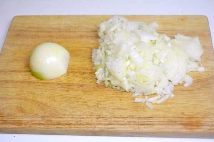 Finely diced yellow onions prepared on a wooden chopping board for sautéing.