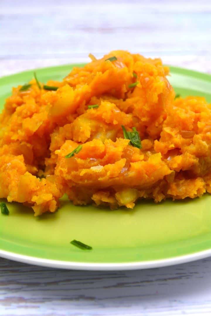 Bowl of rustic caramelized onion mashed potatoes seasoned with sweet Hungarian paprika and fresh chives on a green plate.
