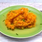 Bowl of rustic caramelized onion mashed potatoes seasoned with sweet Hungarian paprika and fresh chives on a green plate.