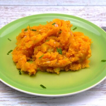 Bowl of rustic caramelized onion mashed potatoes seasoned with sweet Hungarian paprika and fresh chives on a green plate.