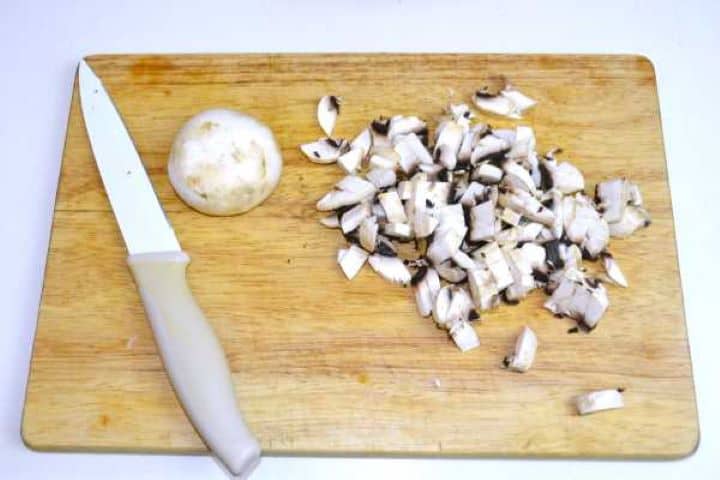 Finely diced fresh portobello mushrooms on a wooden cutting board.