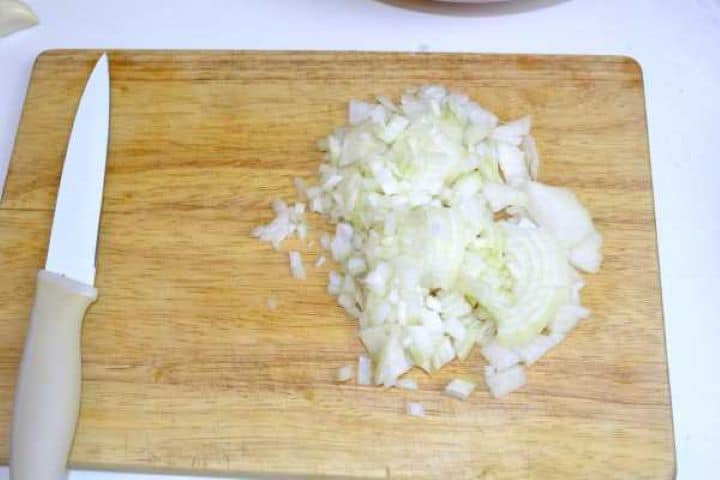 Finely chopped yellow onions prepared for sautéing on a wooden cutting board.