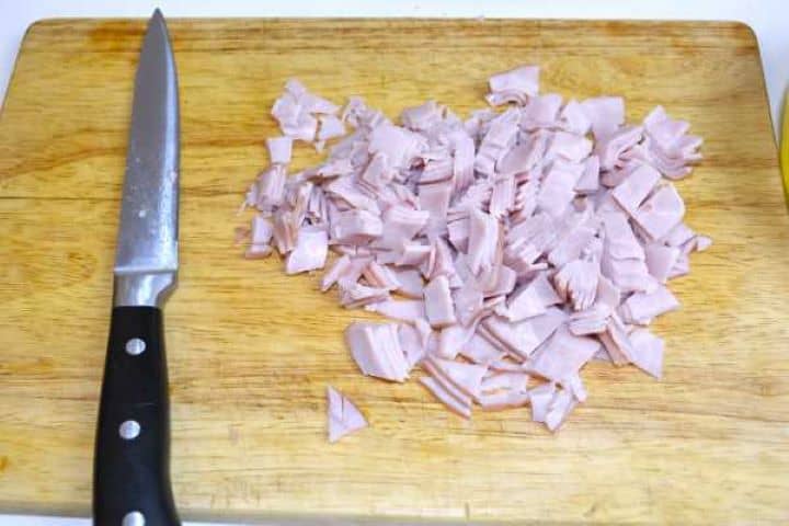 Cubed cooked smoked ham diced into small bite-sized pieces on a cutting board.