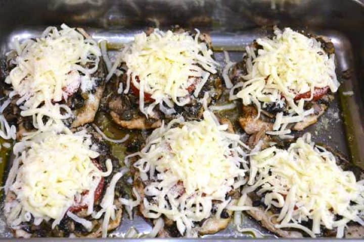 Pork chops topped with thick layers of grated mozzarella and parmesan cheese ready for the oven.