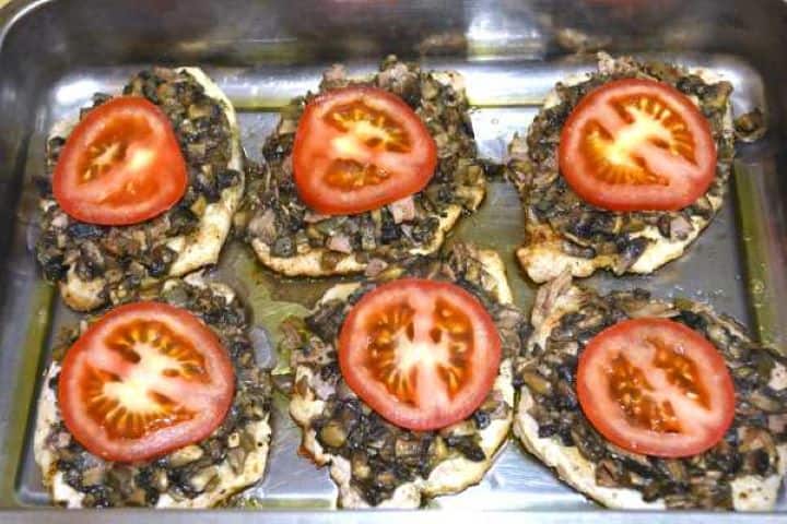 Fresh red tomato slices placed over mushroom-topped pork chops in a baking tray.