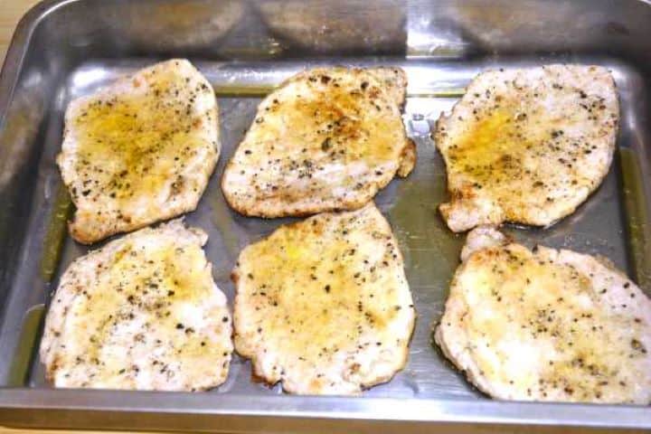 Seared pork chops arranged in a single layer on an olive-oil greased baking tray.