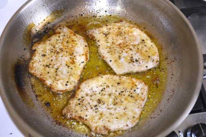 Lightly browned seared pork chops on a frying pan before assembling.