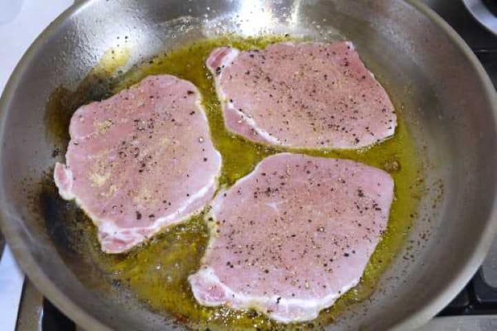 Flash-searing seasoned pork loin chops in a hot skillet with extra virgin olive oil.
