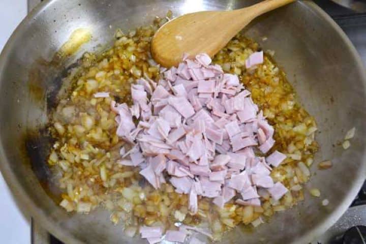 Diced onions and smoked ham sautéing with minced garlic in an olive oil skillet.