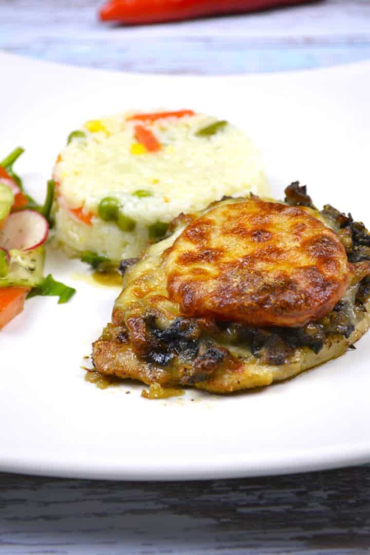 Juicy cheesy pork chops topped with melted mozzarella, served on a white plate with steamed rice and fresh summer salad.