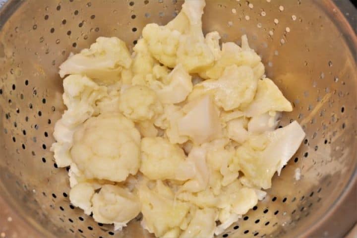 Boiled cauliflower florets draining in a mesh strainer to steam-dry.