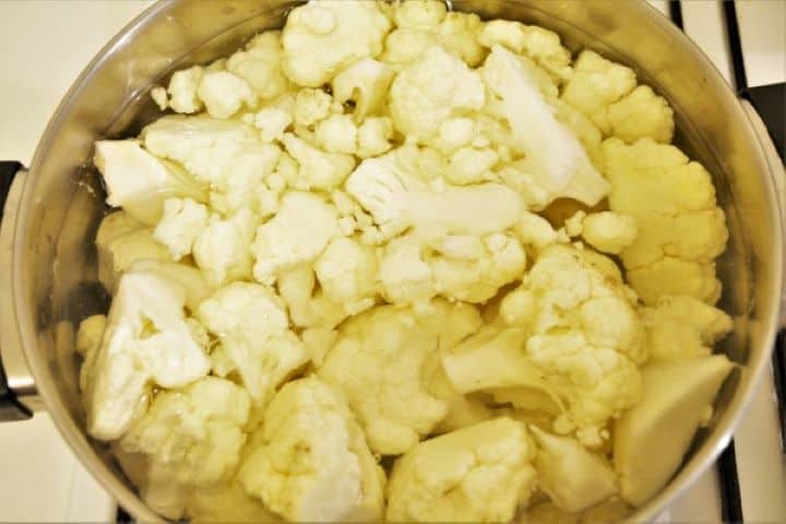 Boiling cauliflower florets in a large pot of salted water with lemon.