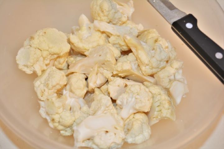 Fresh white cauliflower head broken into even medium florets in a bowl.