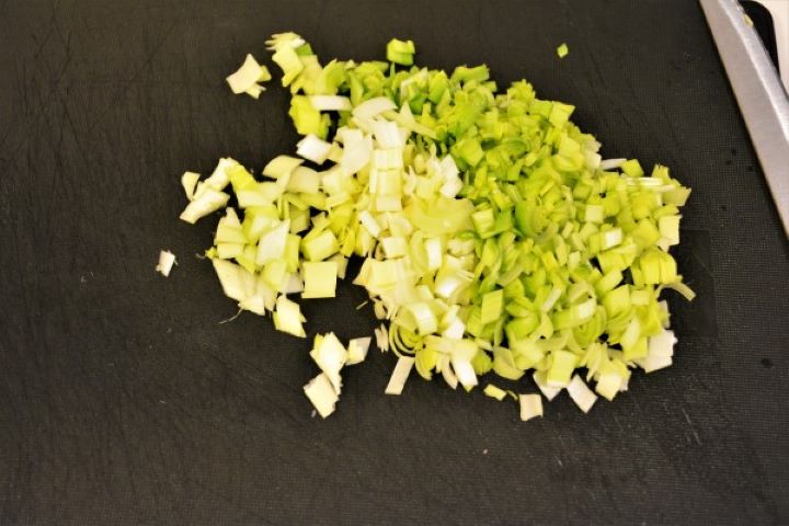 Chopped white and pale green leeks on a black cutting board.